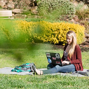 Student working on laptop in the sun outside.