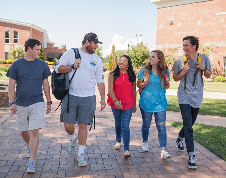 NGU students laugh while walking on a brick path together on campus.